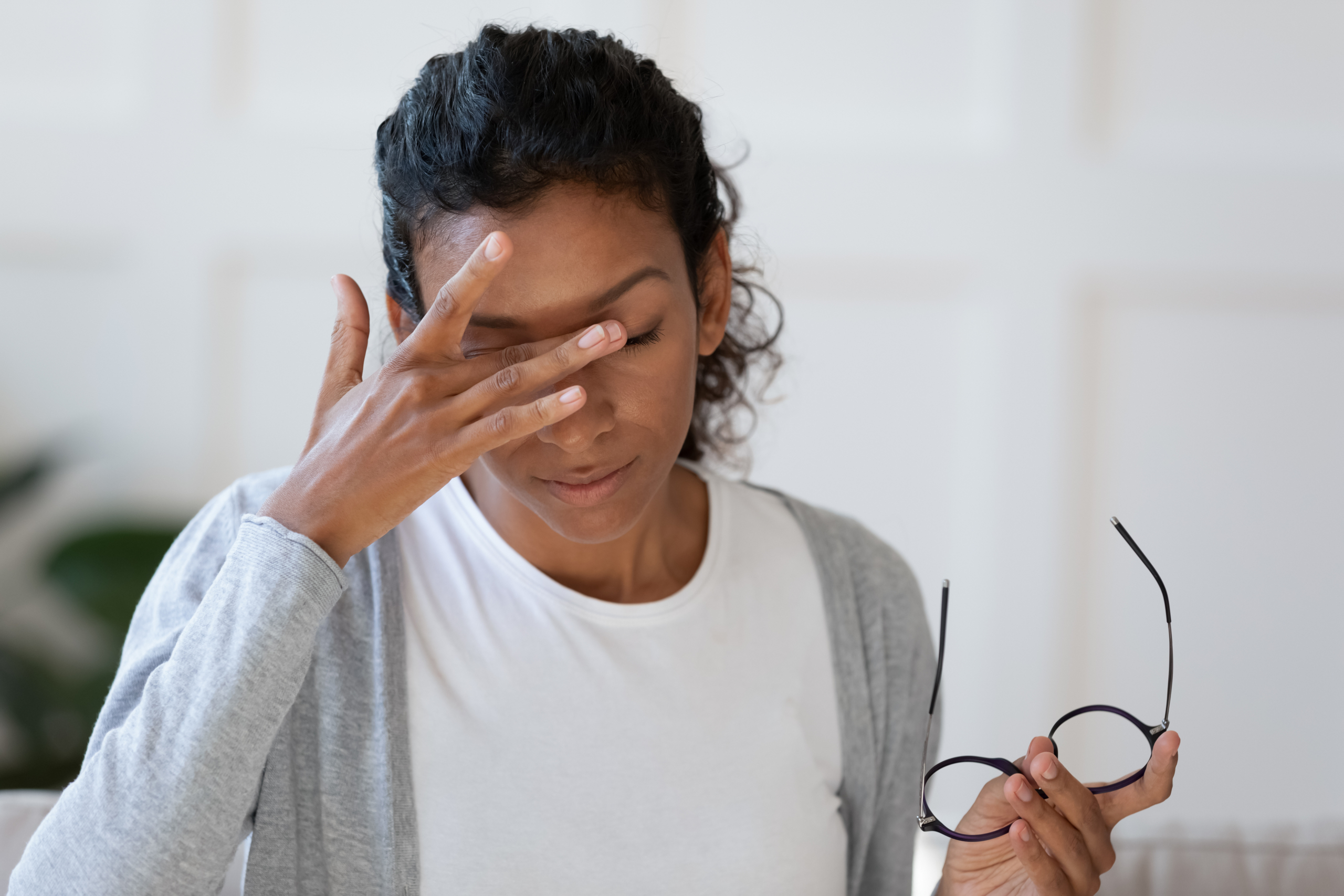 Head shot young stressed unhappy african american woman taking off eyeglasses, feeling tired of long computer work or suffering from dry eyes syndrome, massaging nose bridge, relieving pain.