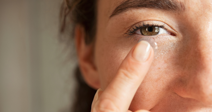 Close up of young woman wearing contact lens with copy space. Young woman holding transparent contact lens on index finger while looking at camera. Close up eye of healthy beautiful girl about to wear contact-lens.