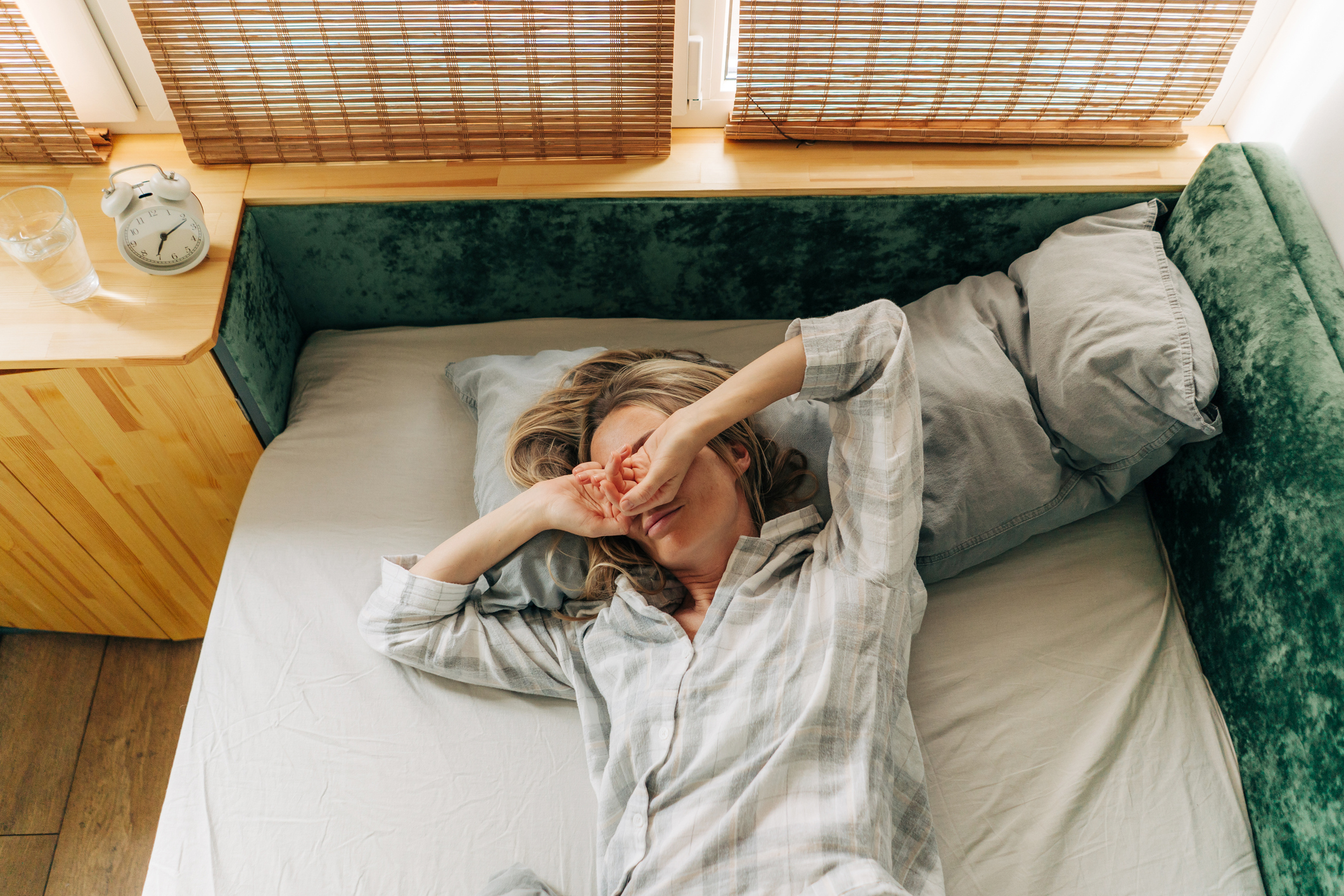 Sleepy woman lying in bed after waking up, stretching and rubbing her eyes.